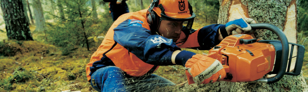 A worker cutting a tree with an orange 2020 Husqvarna Power chainsaw.