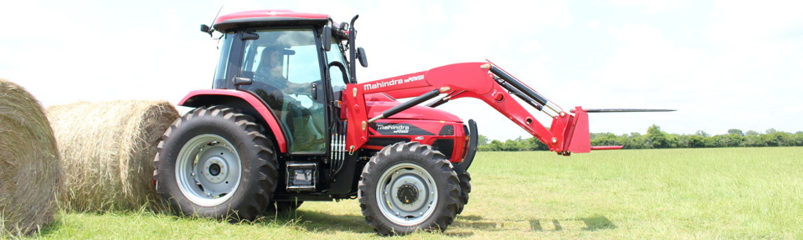 A woman operating a red 2020 Mahindra mPOWER 85P Cab tractor with a front attachment.